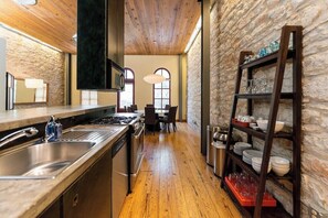 A kitchen with a wooden floor, stainless steel appliances, a wooden ceiling, and a stone wall.