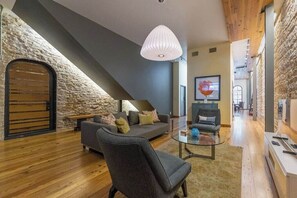 A modern living room with a stone accent wall, a sofa, a chair, and a glass coffee table. - Luxury Stay | Views, Game Room & Chef’s Kitchen (Austin)