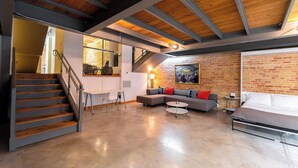 Un amplio espacio tipo loft con una escalera, un gran conjunto de sofás, una mesa de comedor y una zona de cocina.