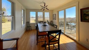 A dining room with a wooden table and chairs, large windows, and a ceiling fan.