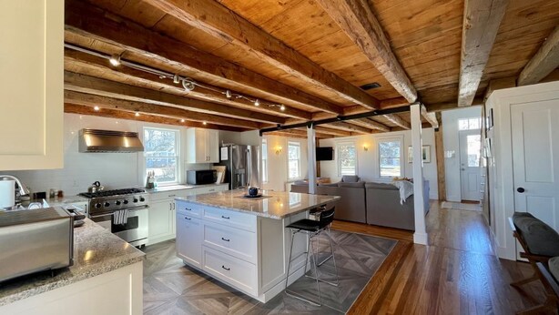 A spacious kitchen with a large island, wooden ceiling beams, and a modern stove.