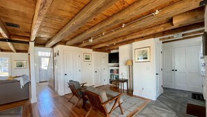 A spacious living area with wooden flooring, a sofa, a coffee table, and a dining table. There are white doors and a television on the wall.