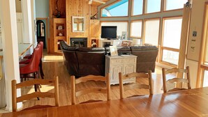 A spacious living area with a wooden ceiling, large windows, a fireplace, and a television. - WH888- Beautiful! With 4 BRs (2 Masters), Private Pool, Hot Tub & Wet Bar! (Corolla)