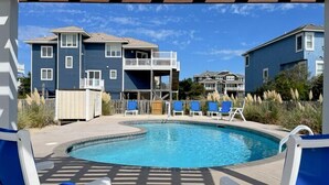 A pool area with blue chairs and a pool, surrounded by buildings with balconies and a clear sky. - WH888- Beautiful! With 4 BRs (2 Masters), Private Pool, Hot Tub & Wet Bar! (Corolla)