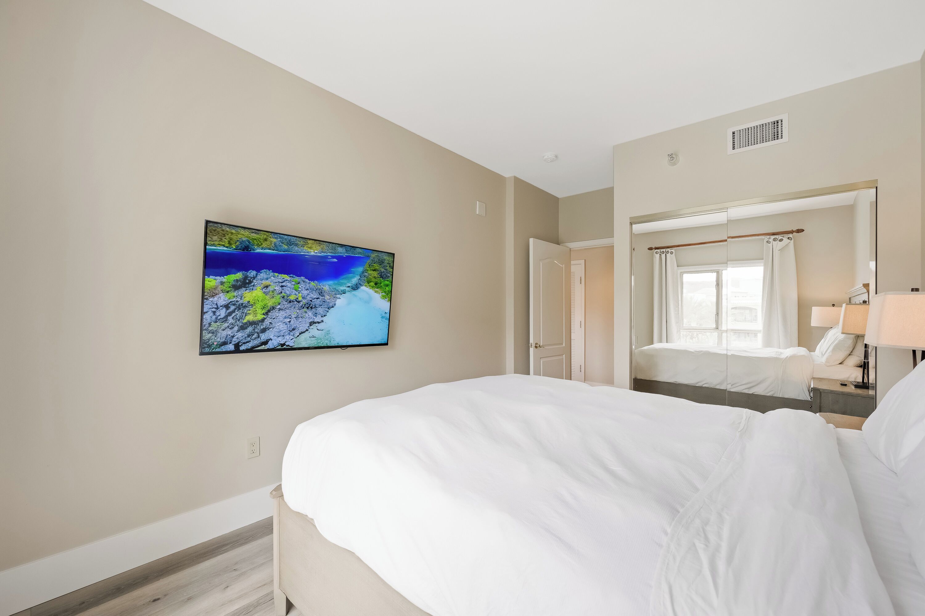 Quarto de hotel com uma cama grande, televisão de tela plana na parede, espelho e janela com cortinas.