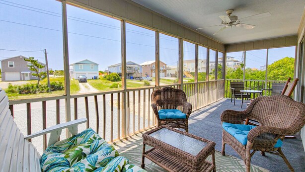 A covered porch with wicker furniture, a ceiling fan, and a view of a residential street. - Merri Mac – Breezy Stays by the Sea (Surf City)