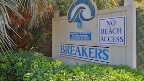 Ein Schild mit der Aufschrift 'PRIVATE PROPERTY – BETRETUNSVERBOT – KEIN ZUGANG ZUM STRAND'. Darunter ein Logo und das Wort 'BREAKERS'.