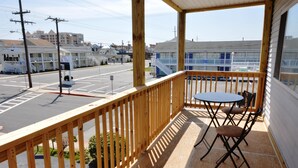 A wooden balcony with a table and chairs, overlooking a street with buildings and a sign for 'Admiral'. - Spacious, quaint 2 bedroom condo with free WiFi and a large balcony located downtown on the bayside just two blocks from the beach! (Ocean City)