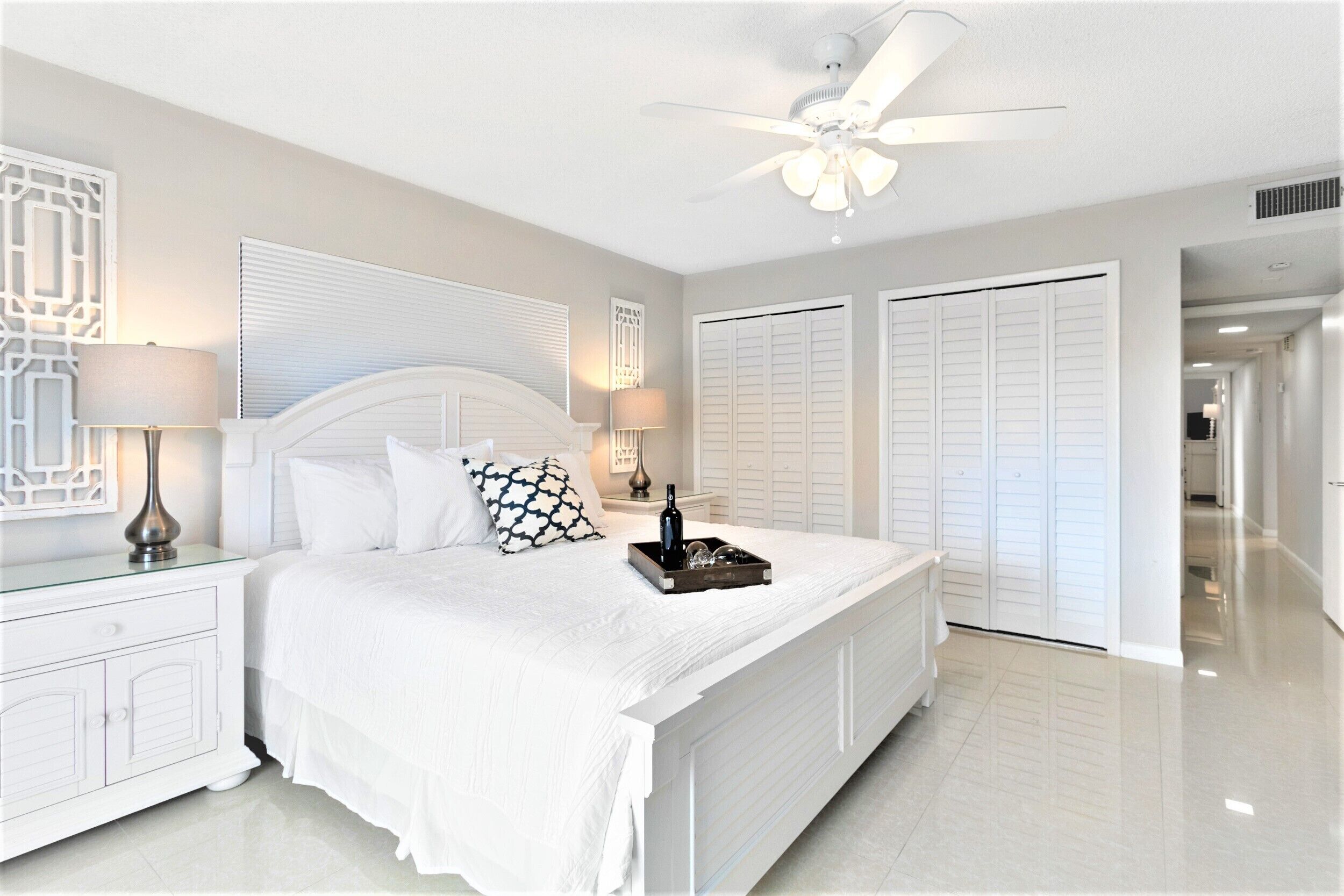 A bedroom with a large bed, white nightstands, a ceiling fan, and white closets.