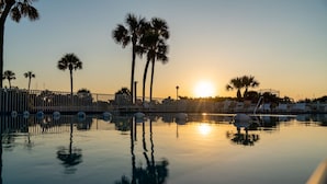 A serene pool area with clear reflections of palm trees and a sunset. - Coastal Family Escape – 3-Bed Retreat w/ Pool, Huge Balcony & Pier Views (Cocoa Beach)