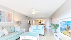 A spacious living room with a light blue sofa, a white coffee table, and a ceiling fan. - Coastal Family Escape – 3-Bed Retreat w/ Pool, Huge Balcony & Pier Views (Cocoa Beach)