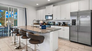 A modern kitchen with white cabinets, stainless steel appliances, a granite countertop, and a bar area with stools. - Stylish Retreat with Great Themed Rooms at Encore (Kissimmee)