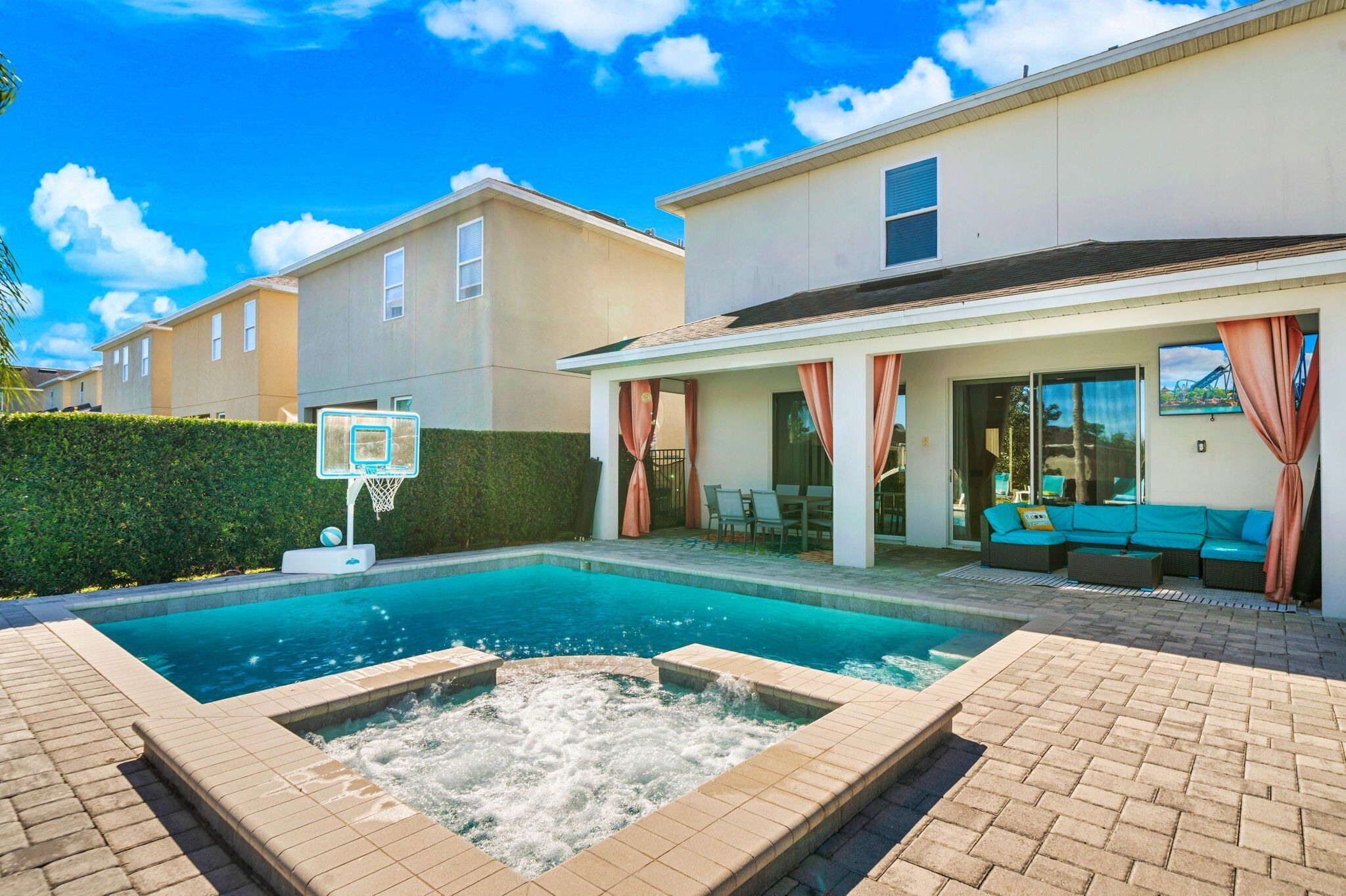 A swimming pool with a hot tub, outdoor seating, and a basketball hoop.