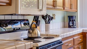 A kitchen with a stove, microwave, and a kettle.