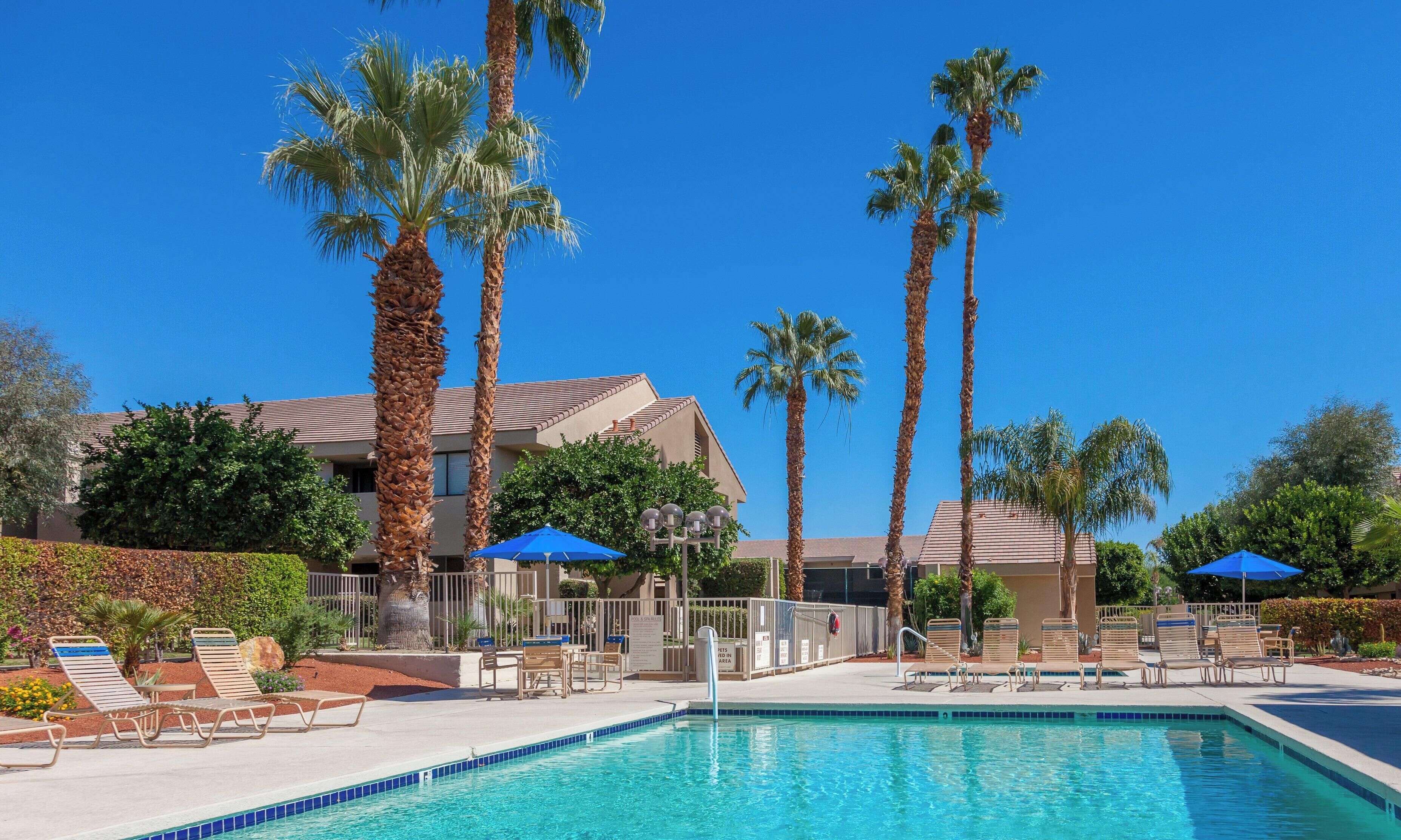 A pool area with lounge chairs, palm trees, and a building in the background.