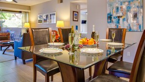 A dining area with a glass table, chairs, and a chandelier. There are bottles and glasses on the table.
