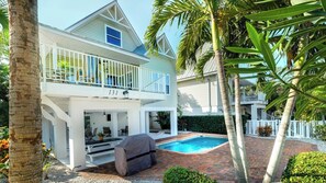 A two-story house with a balcony, a pool, and a covered outdoor seating area.