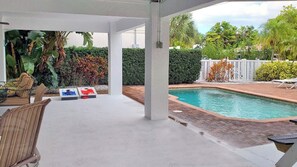 A covered outdoor area with a pool, lounge chairs, and a table with a statue. - Ride the Tide – Heated Pool Home | Steps to Holmes Beach | Heated Pool | Free WIFI & Trolley , NO Roads to Cross, Dog*(See Note)Allow (Holmes Beach)