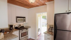 A kitchen with white cabinets, a stainless steel refrigerator, a microwave, a stove, and a washing machine visible through an open door.