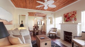A living room with a white fireplace, a ceiling fan, and a dining area.