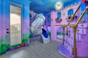 Uma área de recreação com escorrega, escadas e uma parede decorada com tema de castelo.