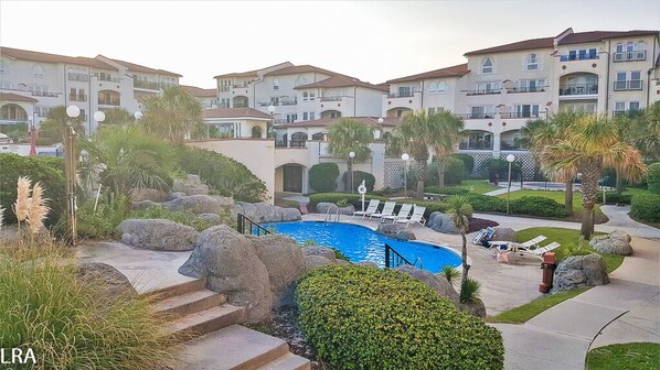 A pool area with lounge chairs, a small pool, and a building with balconies in the background.