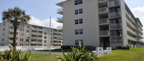 Un edificio residencial de varios pisos con balcones, césped y una palmera.