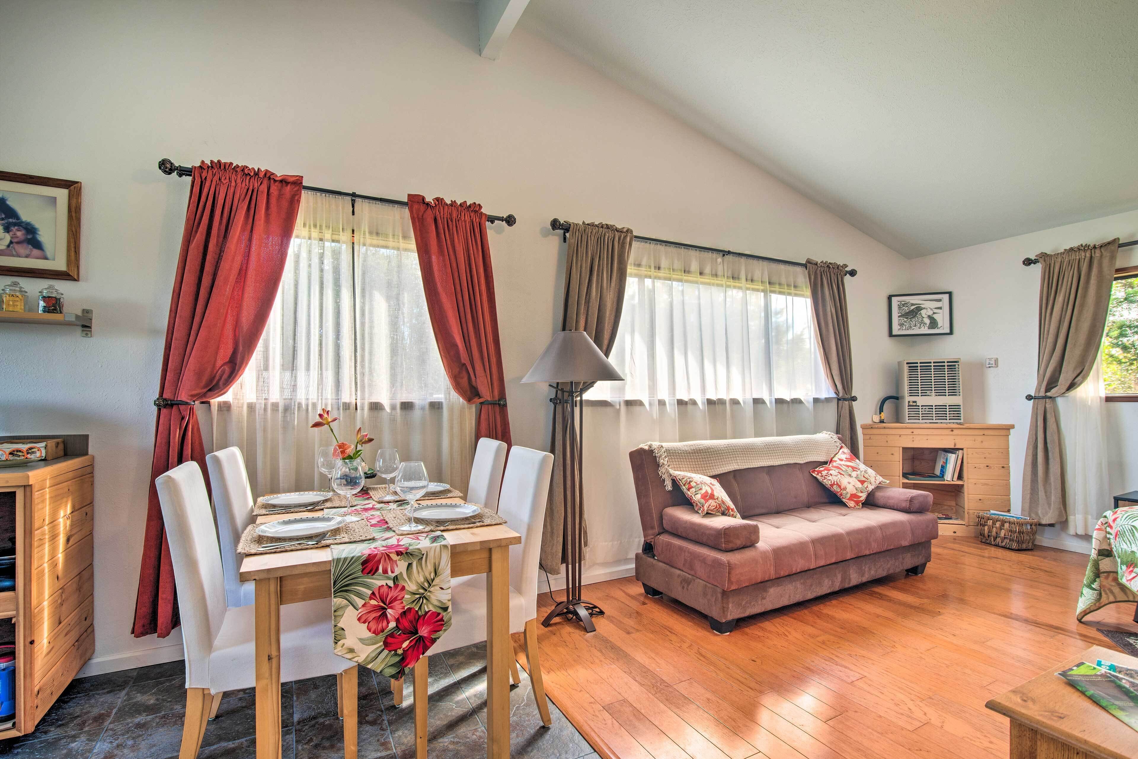 A dining area with a wooden table set for two, a sofa, and a floor lamp.