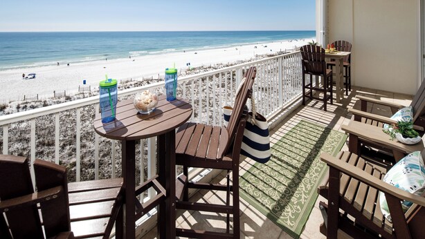 A balcony with wooden furniture, a table with drinks, and a view of the beach. - GD 504 Emerald Sea Oasis: Wake Up to Breathtaking Ocean Views (Fort Walton Beach)