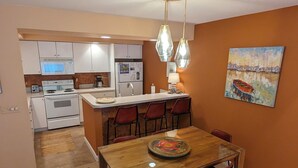 Una cocina compacta con armarios blancos, una isla central con taburetes y una mesa de comedor con sillas.