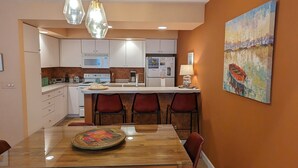 Una cocina moderna con armarios blancos, una isla central con taburetes de bar, una mesa de comedor con sillas y un cuadro en la pared.