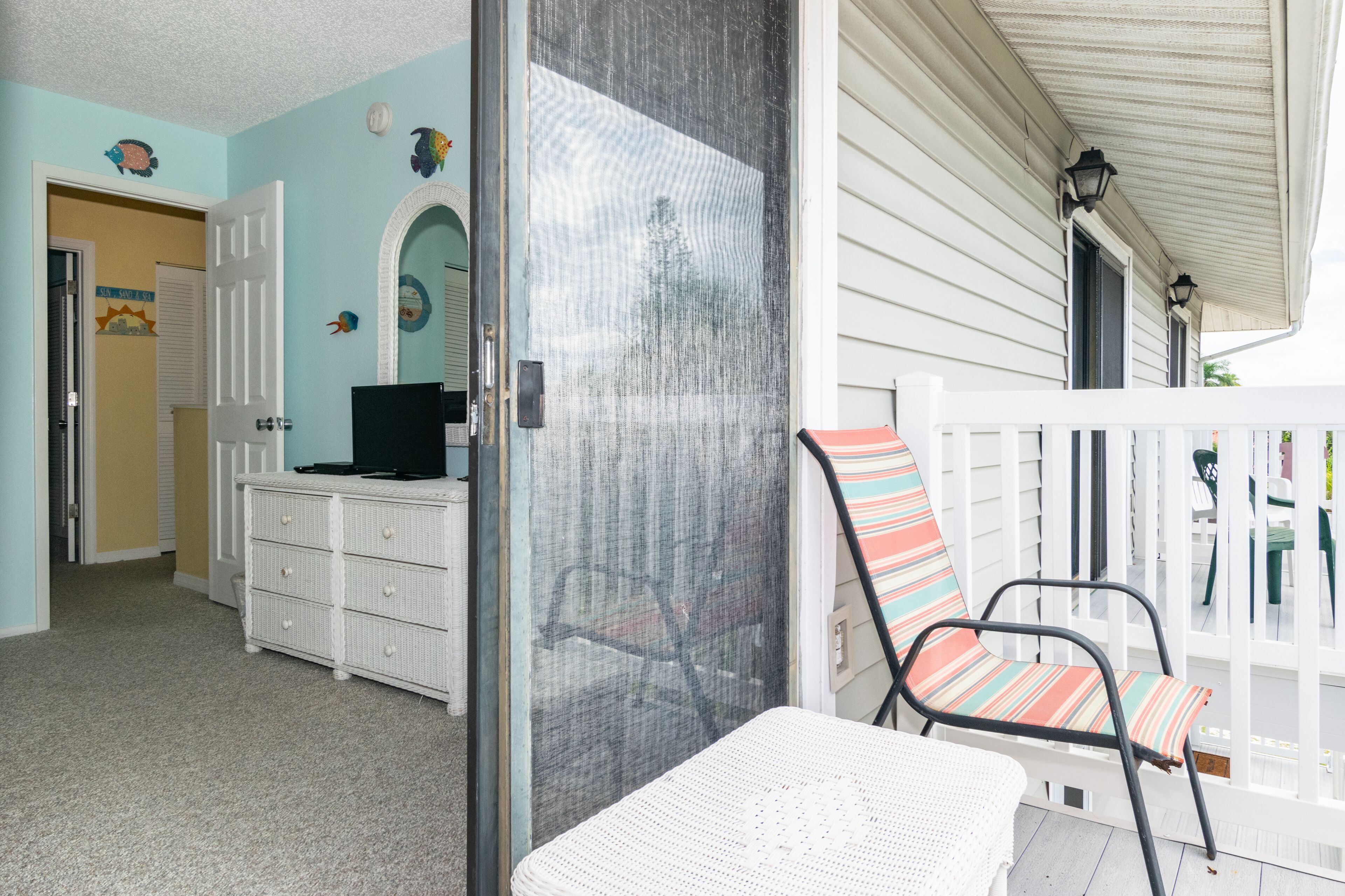A room with a white wicker chair, a white wicker dresser, and a door leading to another room.