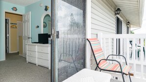 A room with a white wicker chair, a white wicker dresser, and a door leading to another room.