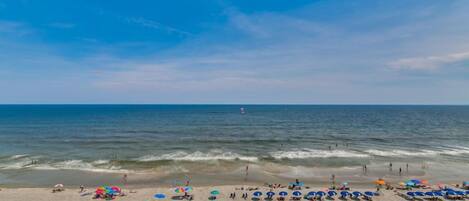 A beach with umbrellas and beach chairs, a wooden walkway, and the ocean.
