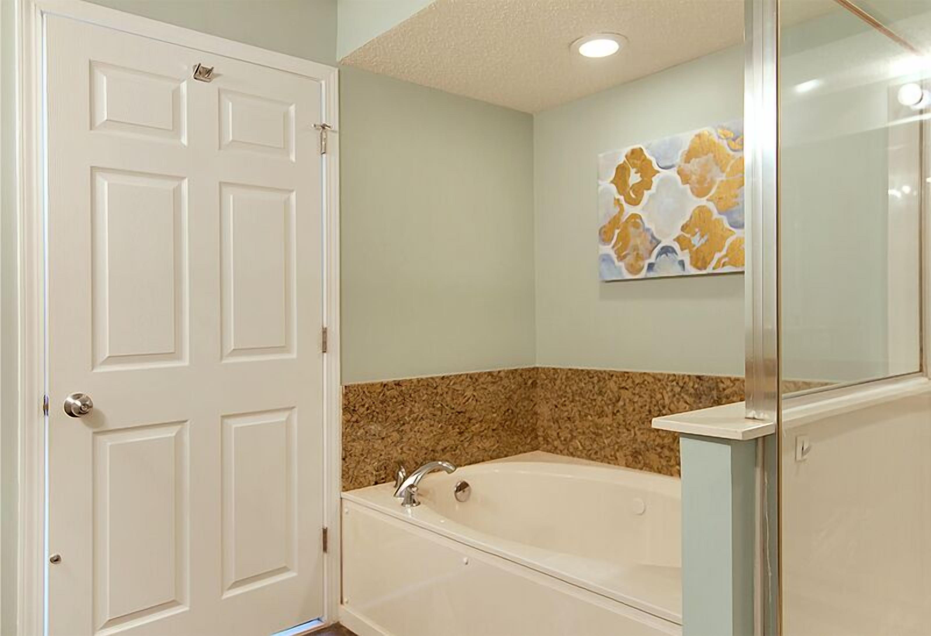 A bathroom with a white bathtub, a granite countertop, and a door with a handle.