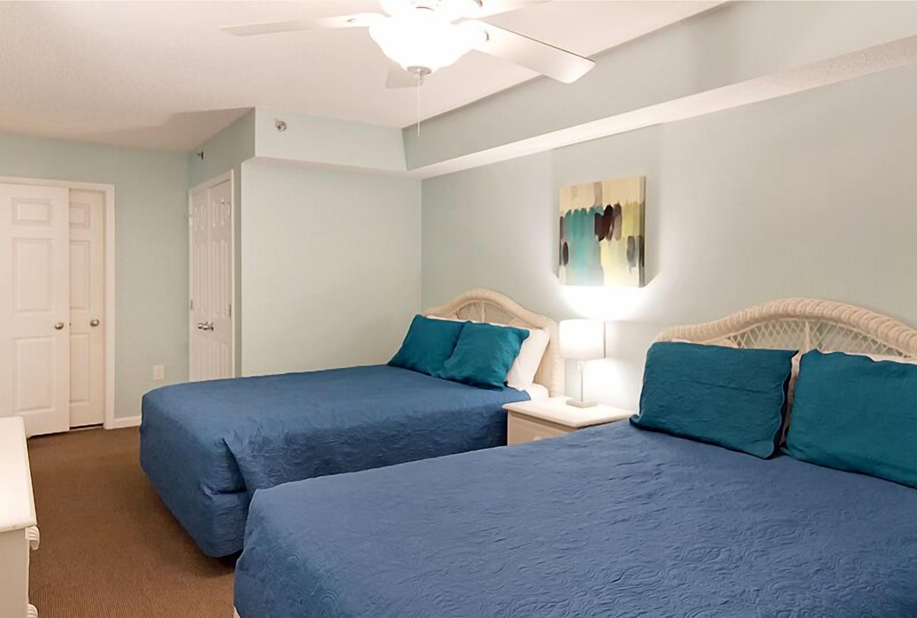 A bedroom with two beds, a ceiling fan, and a painting on the wall.