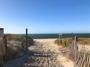 A sandy beach path with wooden fencing on both sides, leading to the ocean.