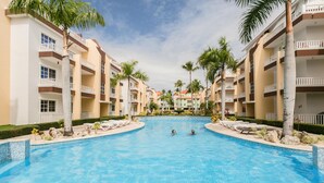 Une piscine entourée d’immeubles à plusieurs étages dotés de balcons, de palmiers et de chaises longues.