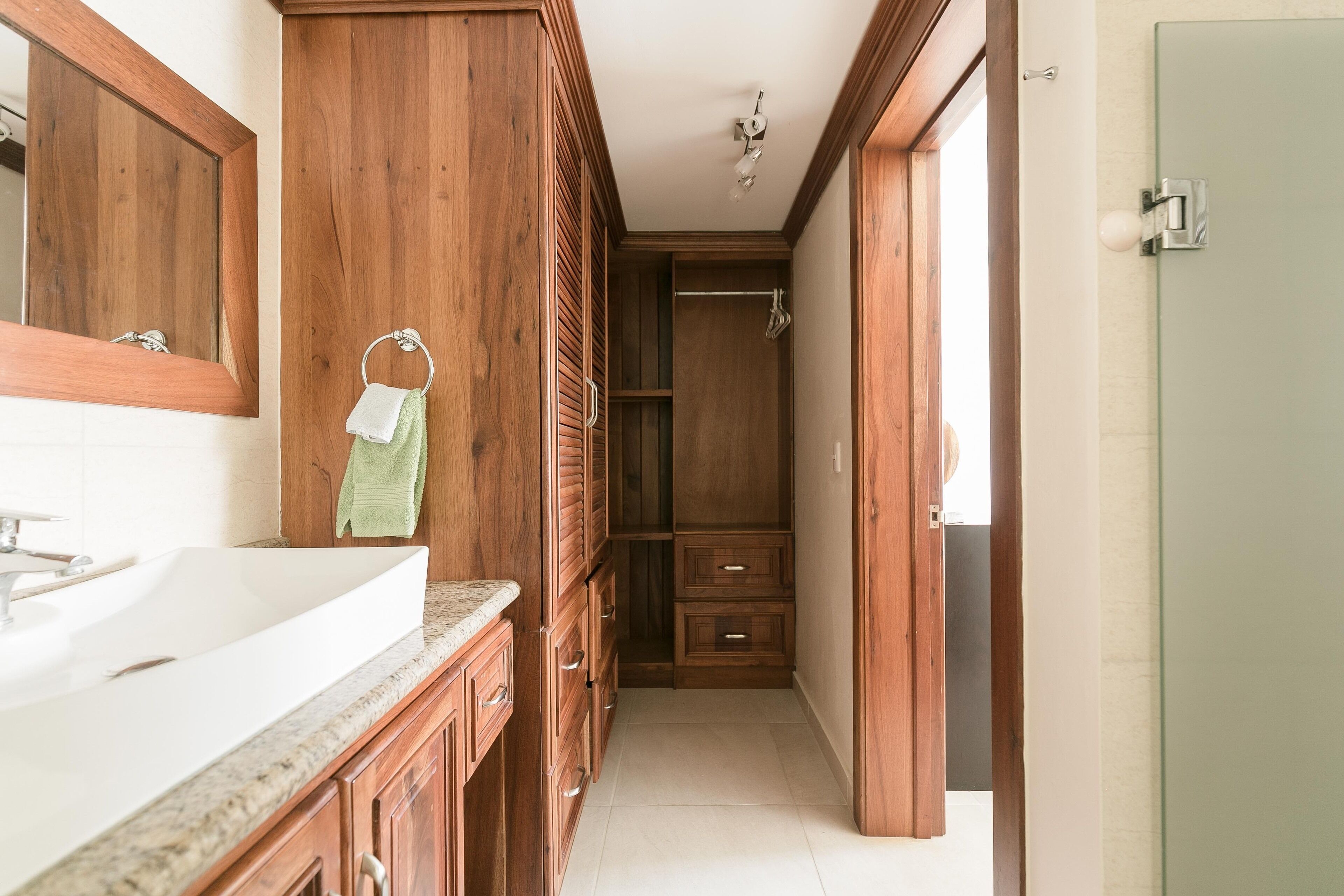 A narrow bathroom with wooden cabinetry, a white sink, and a towel hanging on the wall.