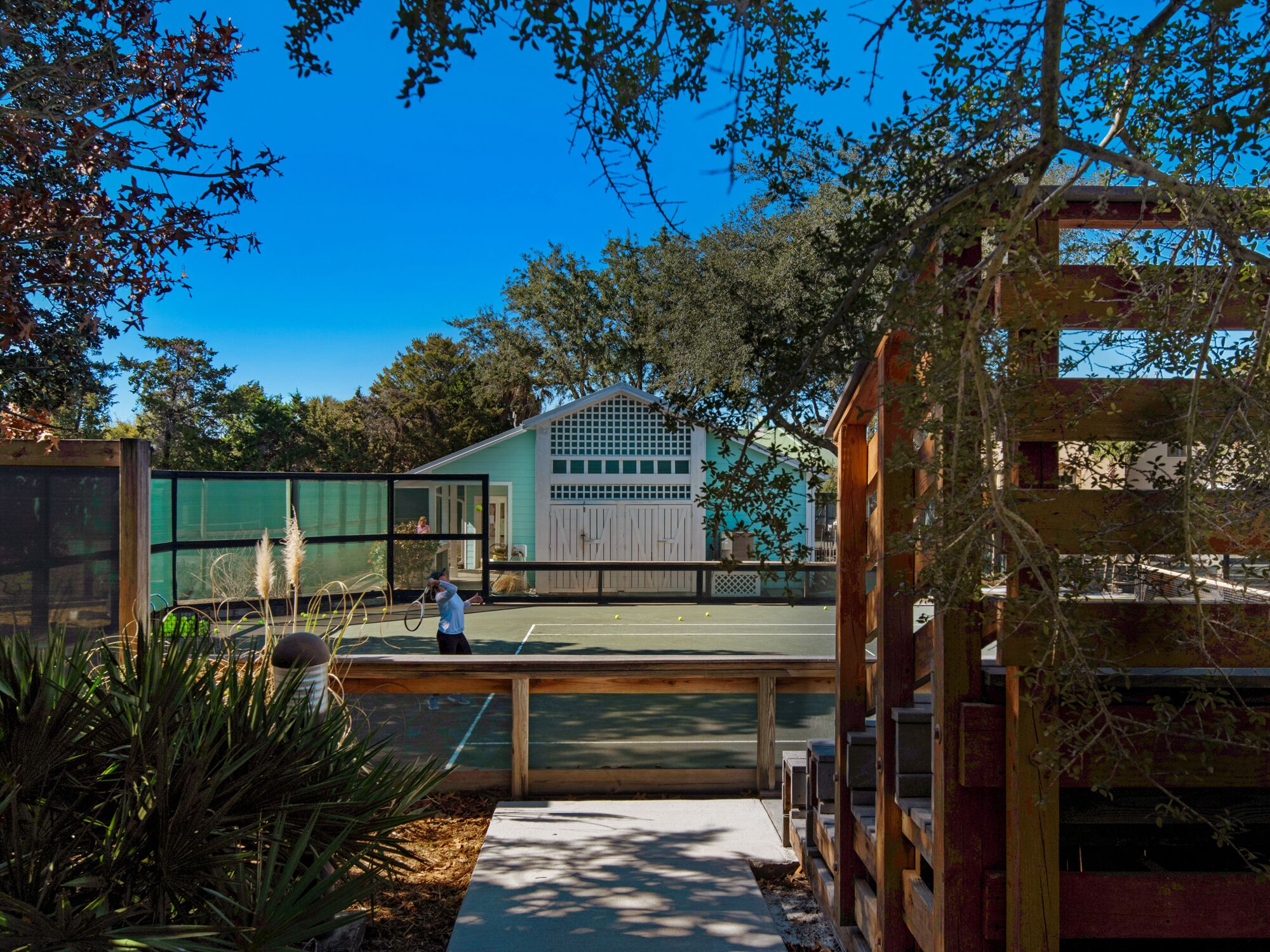 A tennis court with a wooden fence, a house in the background, and trees around.