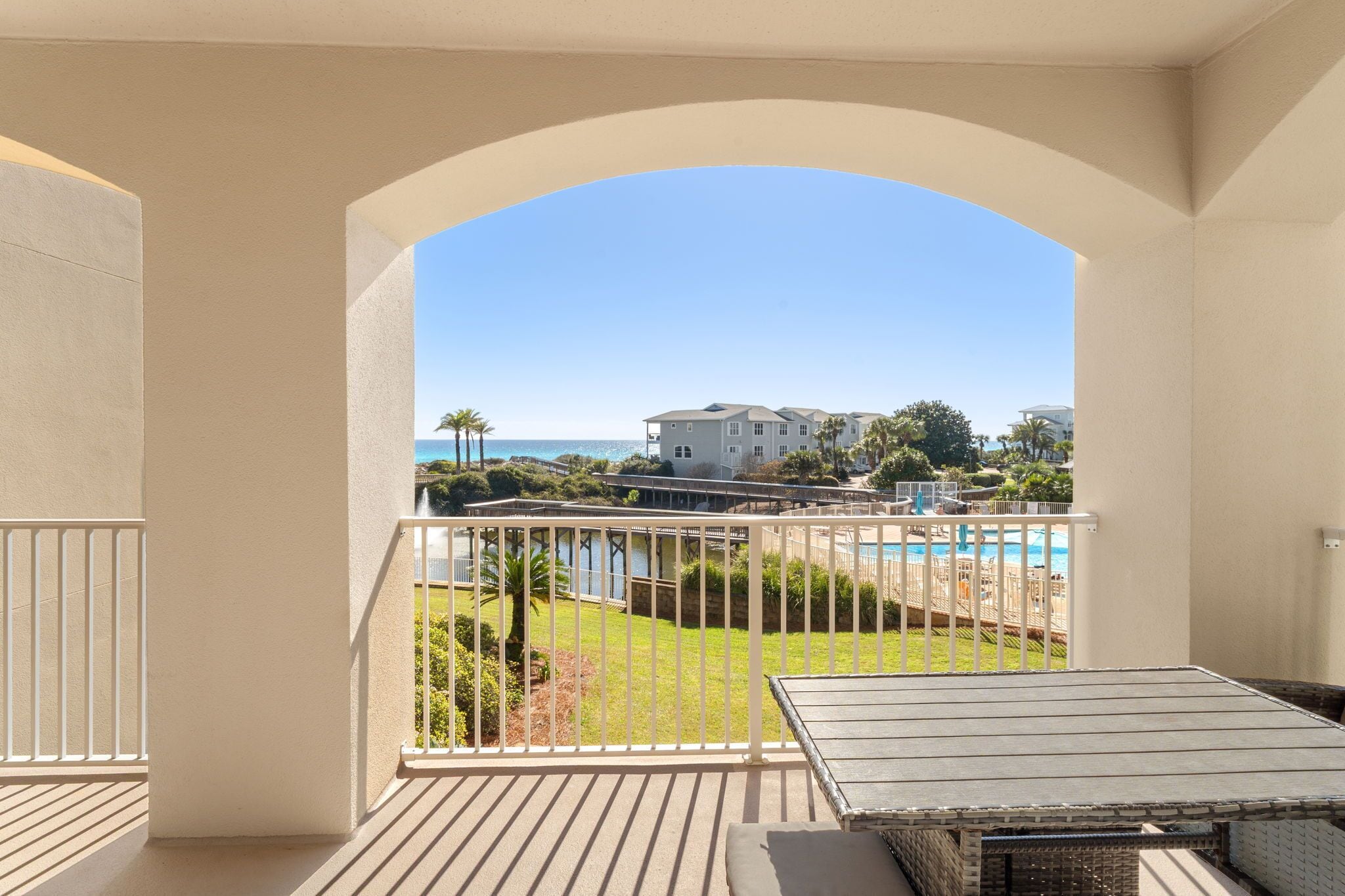 A balcony with a view of a pool, a lawn, and a building across the water.