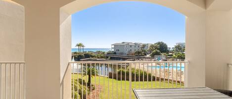 A balcony with a view of a pool, a lawn, and a building across the water.