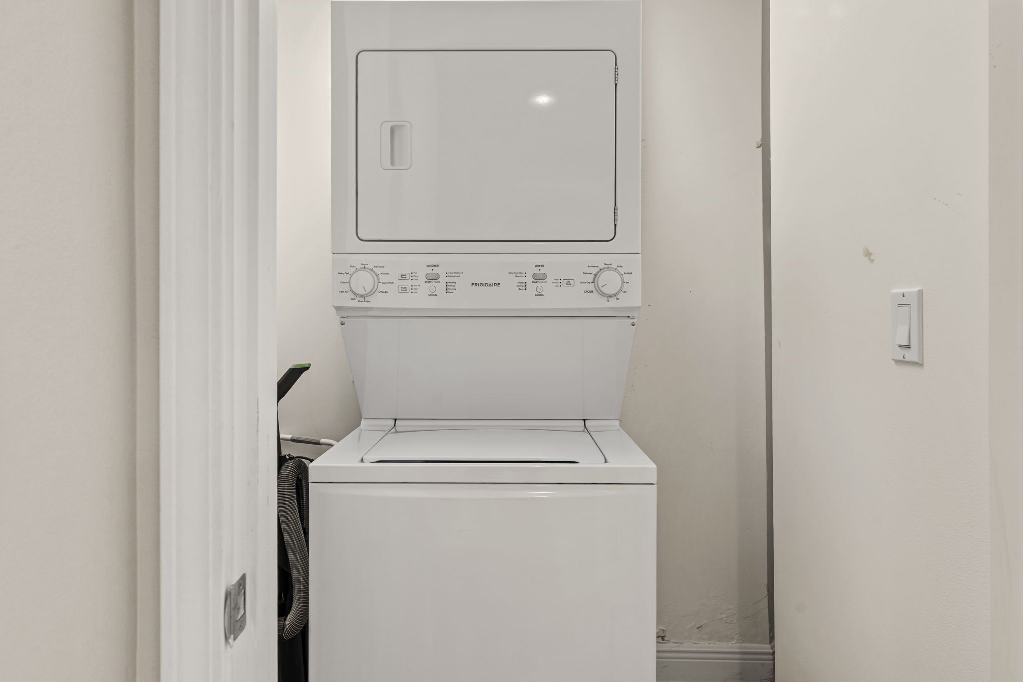 A compact laundry room with a front-loading washer and dryer, a control panel with various settings, and a door leading to another room.