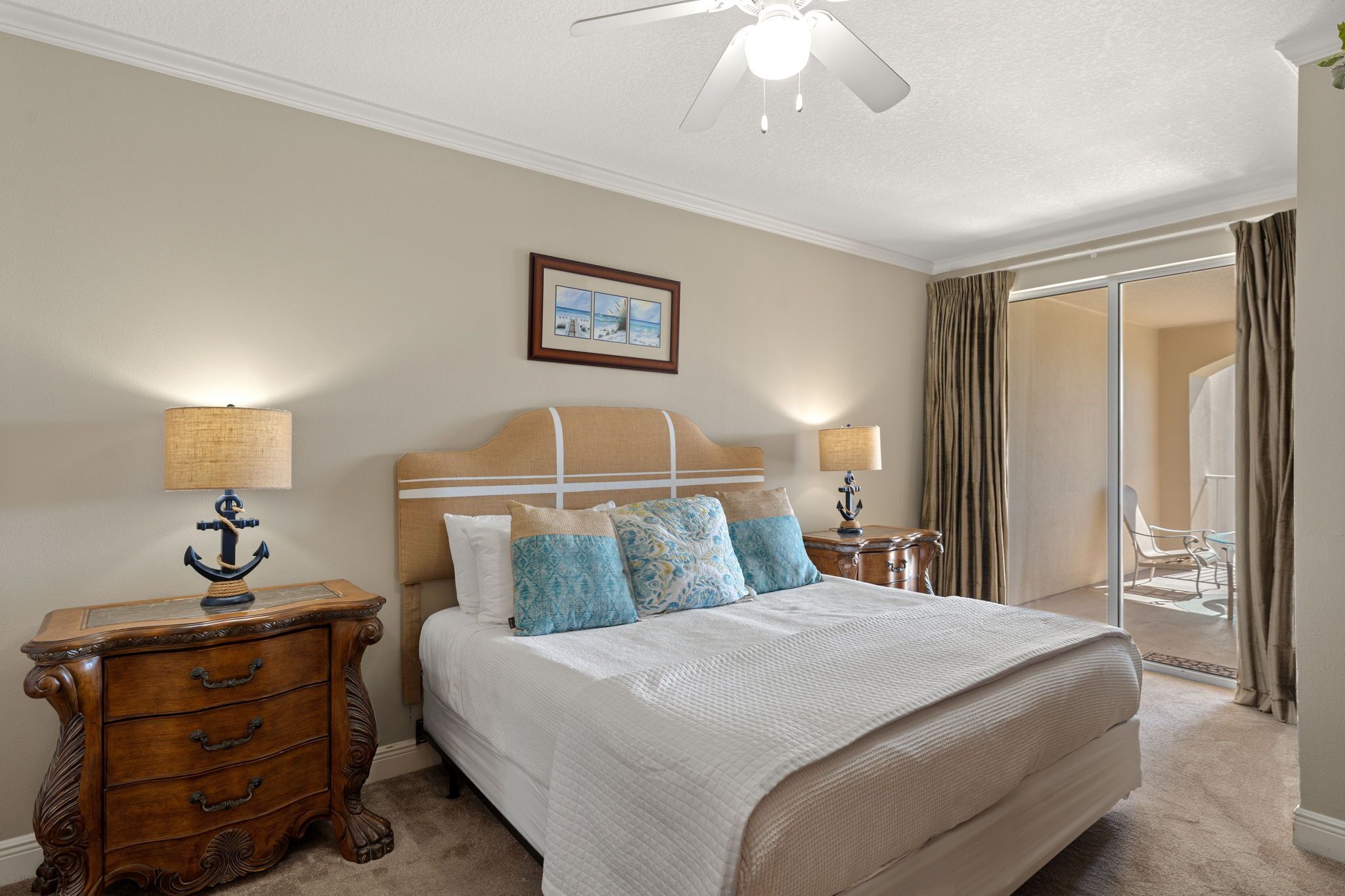 A bedroom with a bed, nightstands, a ceiling fan, and a sliding glass door to a balcony.