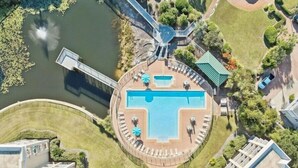 En vy från ovan av ett hotell med en central pool, en bro och omgivande grönska.