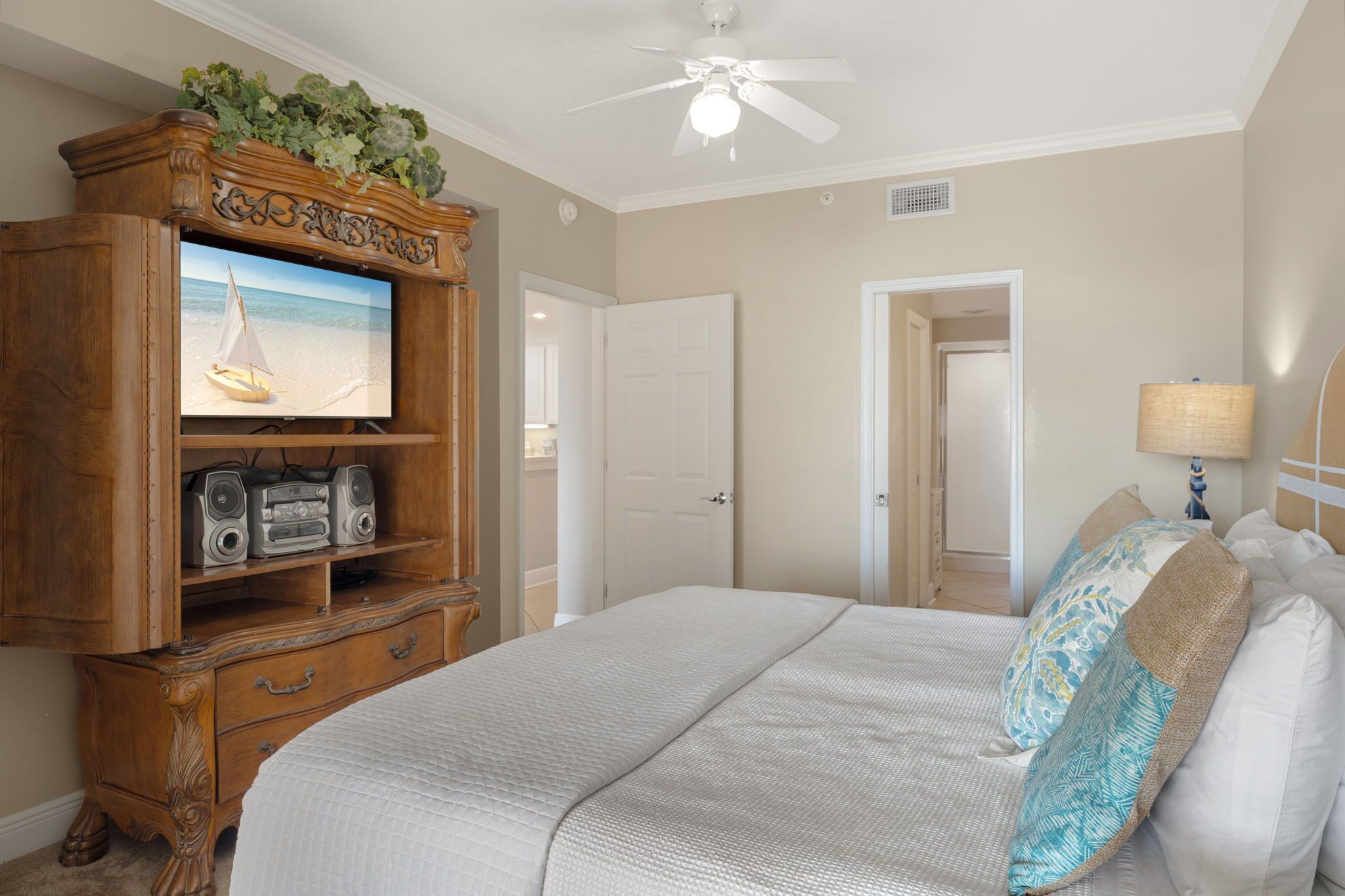 A bedroom with a large bed, a wooden dresser with a television, and a ceiling fan.