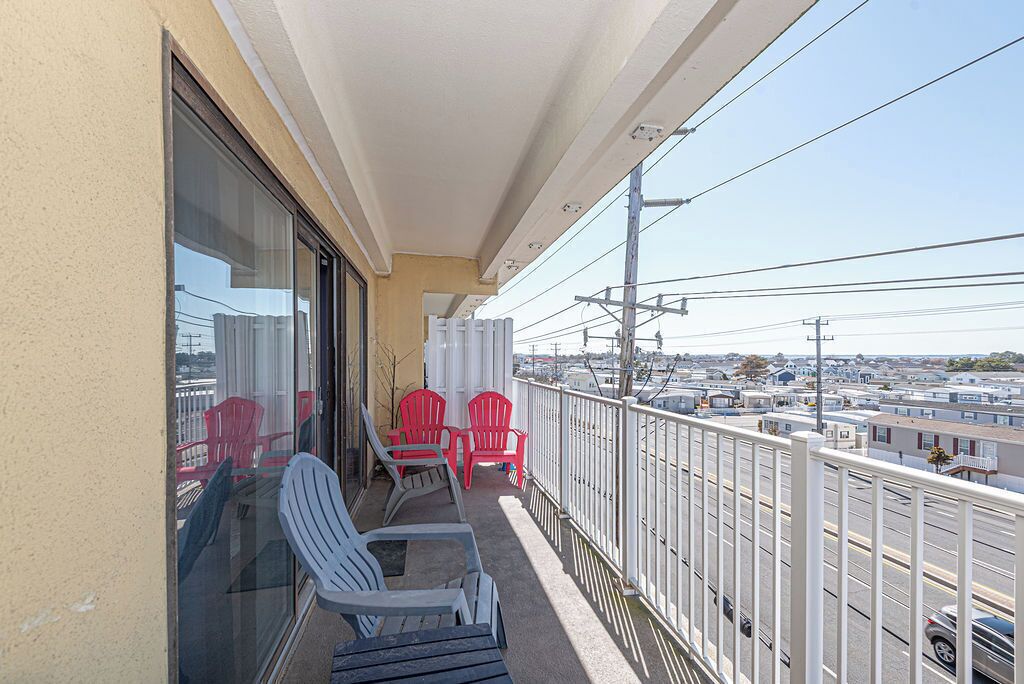 A balcony with chairs, a table, and a view of a parking lot and buildings.
