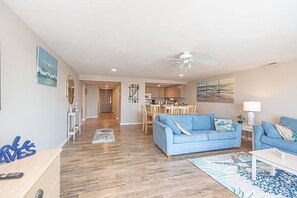 A living room with a blue sofa, a dining area, and a kitchen in the background. - Stylish, spacious 2 bedroom condo with free WiFi, an indoor pool, and HBO channels located uptown near mini golf and movie theater and only a block to the beach! (Ocean City)