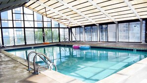 Una piscina interna con acqua limpida, un solarium piastrellato e una zona coperta con ampie finestre.