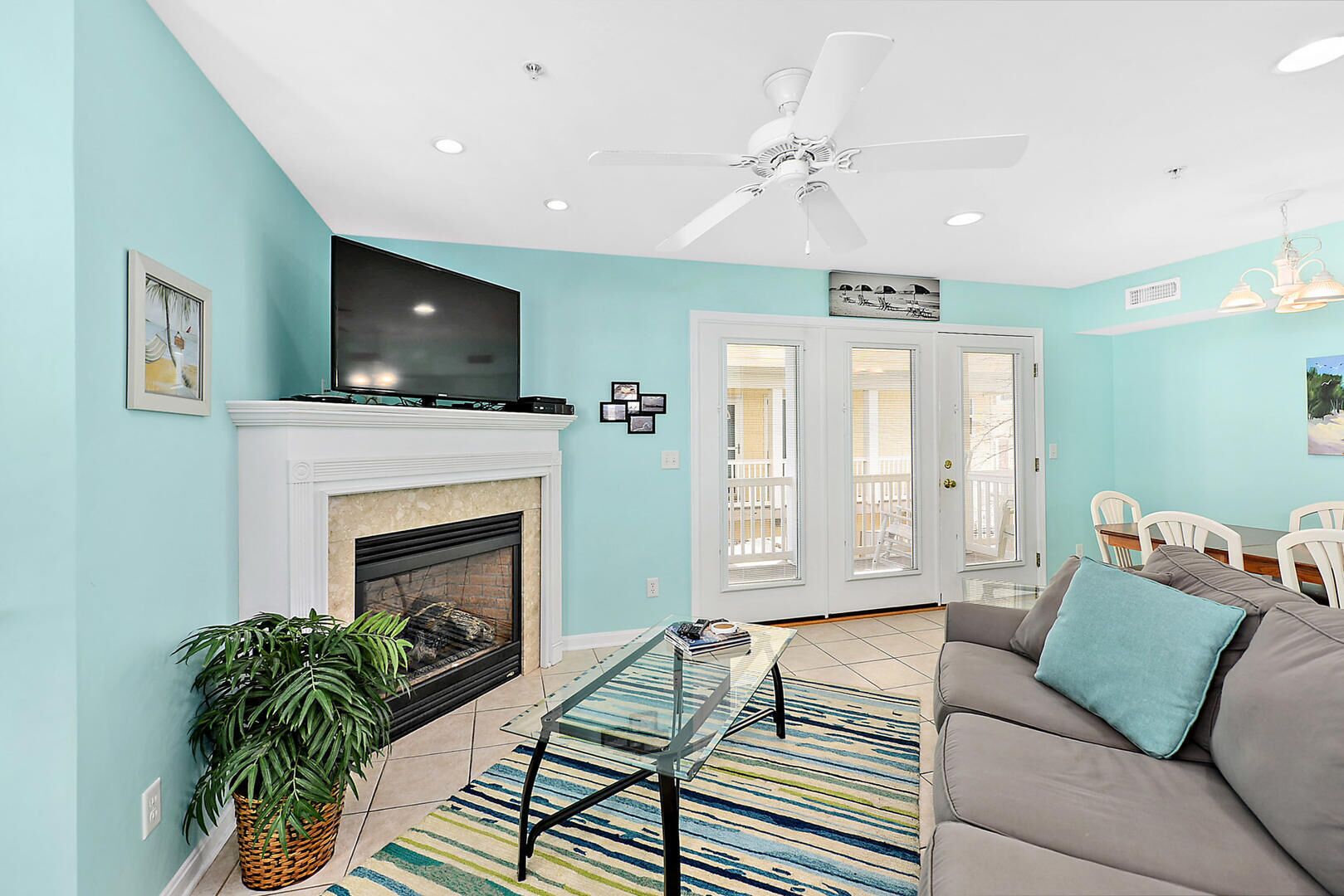 A living room with a fireplace, a ceiling fan, and a dining area with chairs.